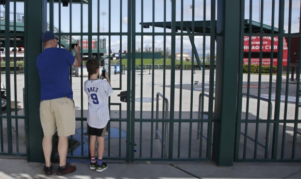 FILE - Cubs fans take photos through the locked gates at Sloan Park, the spring training site of th...