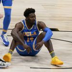UCLA forward Kenneth Nwuba sits on the court after taking a charging call during the second half of an Elite 8 game against Michigan in the NCAA men's college basketball tournament at Lucas Oil Stadium, Tuesday, March 30, 2021, in Indianapolis. (AP Photo/Michael Conroy)