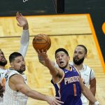 Phoenix Suns guard Devin Booker (1) misses a shot as he gets between Orlando Magic center Nikola Vucevic, left, and guard Evan Fournier, right, as time expired in the second half of an NBA basketball game, Wednesday, March 24, 2021, in Orlando, Fla. (AP Photo/John Raoux)