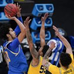 UCLA guard Johnny Juzang, left, shoots over Michigan guard Eli Brooks (55) and forward Brandon Johns Jr., right, during the second half of an Elite 8 game in the NCAA men's college basketball tournament at Lucas Oil Stadium, Tuesday, March 30, 2021, in Indianapolis. (AP Photo/Michael Conroy)