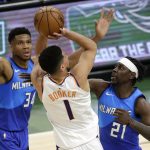 Phoenix Suns' Devin Booker, center, is fouled as he shoots between Milwaukee Bucks' Jrue Holiday, right, and Giannis Antetokounmpo, left, during the first half of an NBA basketball game Monday, April 19, 2021, in Milwaukee. (AP Photo/Aaron Gash)