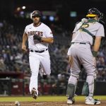 Arizona Diamondbacks' Madison Bumgarner, left, scores a run as Oakland Athletics catcher Sean Murphy waits for a possible throw during the third inning of a baseball game Monday, April 12, 2021, in Phoenix. (AP Photo/Ross D. Franklin)