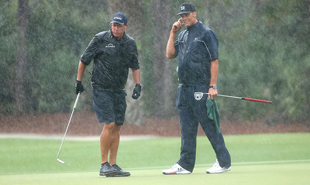 Phil Mickelson and NFL player Tom Brady of the Tampa Bay Buccaneers stand in the rain on the 13th g...