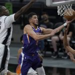 Phoenix Suns guard Devin Booker (1) drives to the basket past San Antonio Spurs center Gorgui Dieng (7) and guard Devin Vassell (24) during the first half of an NBA basketball game in San Antonio, Saturday, May 15, 2021. (AP Photo/Eric Gay)