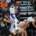 Los Angeles Lakers guard Dennis Schroder, right, leaps into the crowd to get a loose ball as Phoenix Suns guard Cameron Payne (15) looks on during the second half of Game 1 of their NBA basketball first-round playoff series Sunday, May 23, 2021, in Phoenix. The Suns defeated the Lakers 99-90. (AP Photo/Ross D. Franklin)