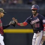 Washington Nationals' Victor Robles, right, playfully slaps the glove of Arizona Diamondbacks third baseman Eduardo Escobar, left, after Robles started running to third base on a foul ball during the third inning of a baseball game Sunday, May 16, 2021, in Phoenix. (AP Photo/Ross D. Franklin)