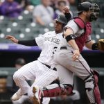 Colorado Rockies' Elias Diaz, back, slides safely into home plate to score on a single hit by Raimel Tapia as Arizona Diamondbacks catcher Stephen Vogt looks for the throw in the third inning of a baseball game Saturday, May 22, 2021, in Denver. (AP Photo/David Zalubowski)