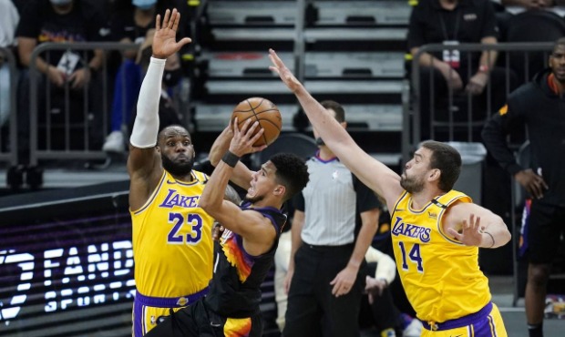 Phoenix Suns guard Devin Booker, middle, gets off a shot over Los Angeles Lakers forward LeBron Jam...