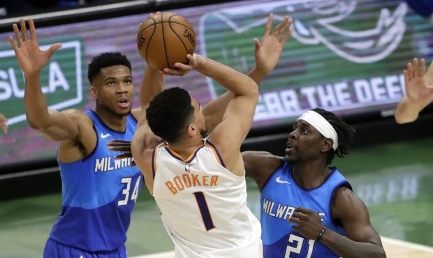 Phoenix Suns' Devin Booker, center, is fouled as he shoots between Milwaukee Bucks' Jrue Holiday, r...