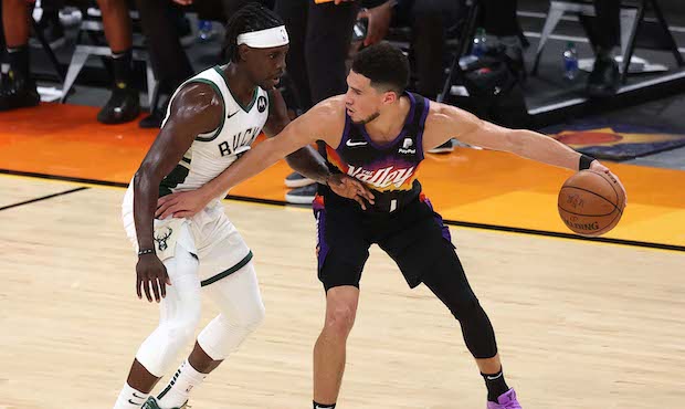 Jrue Holiday #21 of the Milwaukee Bucks defends as Devin Booker #1 of the Phoenix Suns brings the b...