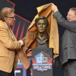 Tom Flores, a member of the Pro Football Hall of Fame Class of 2021, left, and his presenter Las Vegas Raiders owner Mark Davis unveil the bust during the induction ceremony at the Pro Football Hall of Fame, Sunday, Aug. 8, 2021, in Canton, Ohio. (AP Photo/David Richard)