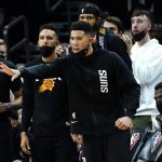 Phoenix Suns guard Devin Booker cheers fro the bench during the second half of an NBA basketball game against the Golden State Warriors, Tuesday, Nov. 30, 2021, in Phoenix. Booker did not play in the second half. The Suns won 104-96. (AP Photo/Matt York)
