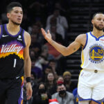 Golden State Warriors guard Stephen Curry reacts after scoring against Phoenix Suns guard Devin Booker (1) during the first half of an NBA basketball game Saturday, Dec. 25, 2021, in Phoenix. (AP Photo/Rick Scuteri)