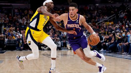 Devin Booker #1 of the Phoenix Suns dribbles the ball while being guarded by Justin Holiday #8 of t...