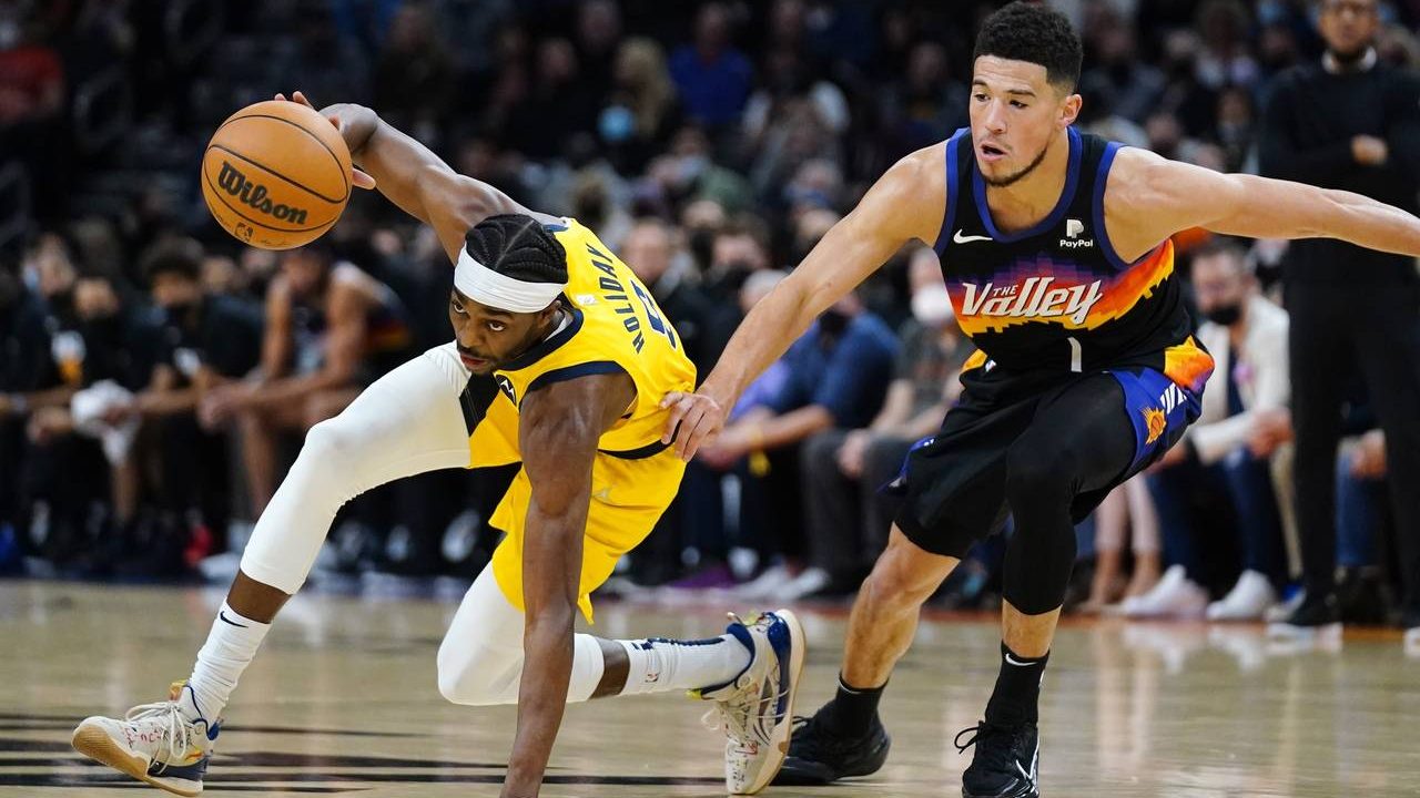 Indiana Pacers forward Justin Holiday, left, dribbles around Phoenix Suns guard Devin Booker (1) du...