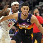 Phoenix Suns guard Devin Booker (1) drives past Los Angeles Clippers guard Eric Bledsoe during the first half of an NBA basketball game Thursday, Jan. 6, 2022, in Phoenix. (AP Photo/Rick Scuteri)