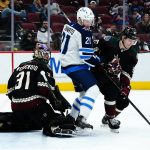 Arizona Coyotes defenseman Vladislav Kolyachonok (92) tries to control the puck in front of Winnipeg Jets center Dominic Toninato (21) and Coyotes goaltender Scott Wedgewood (31) during the second period of an NHL hockey game Sunday, Feb. 27, 2022, in Glendale, Ariz. (AP Photo/Ross D. Franklin)