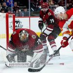 Arizona Coyotes goaltender Karel Vejmelka (70) makes a save as Calgary Flames center Trevor Lewis (22) waits for a rebound, and Coyotes defenseman Kyle Capobianco (75) watches during the second period of an NHL hockey game Wednesday, Feb. 2, 2022, in Glendale, Ariz. (AP Photo/Ross D. Franklin)