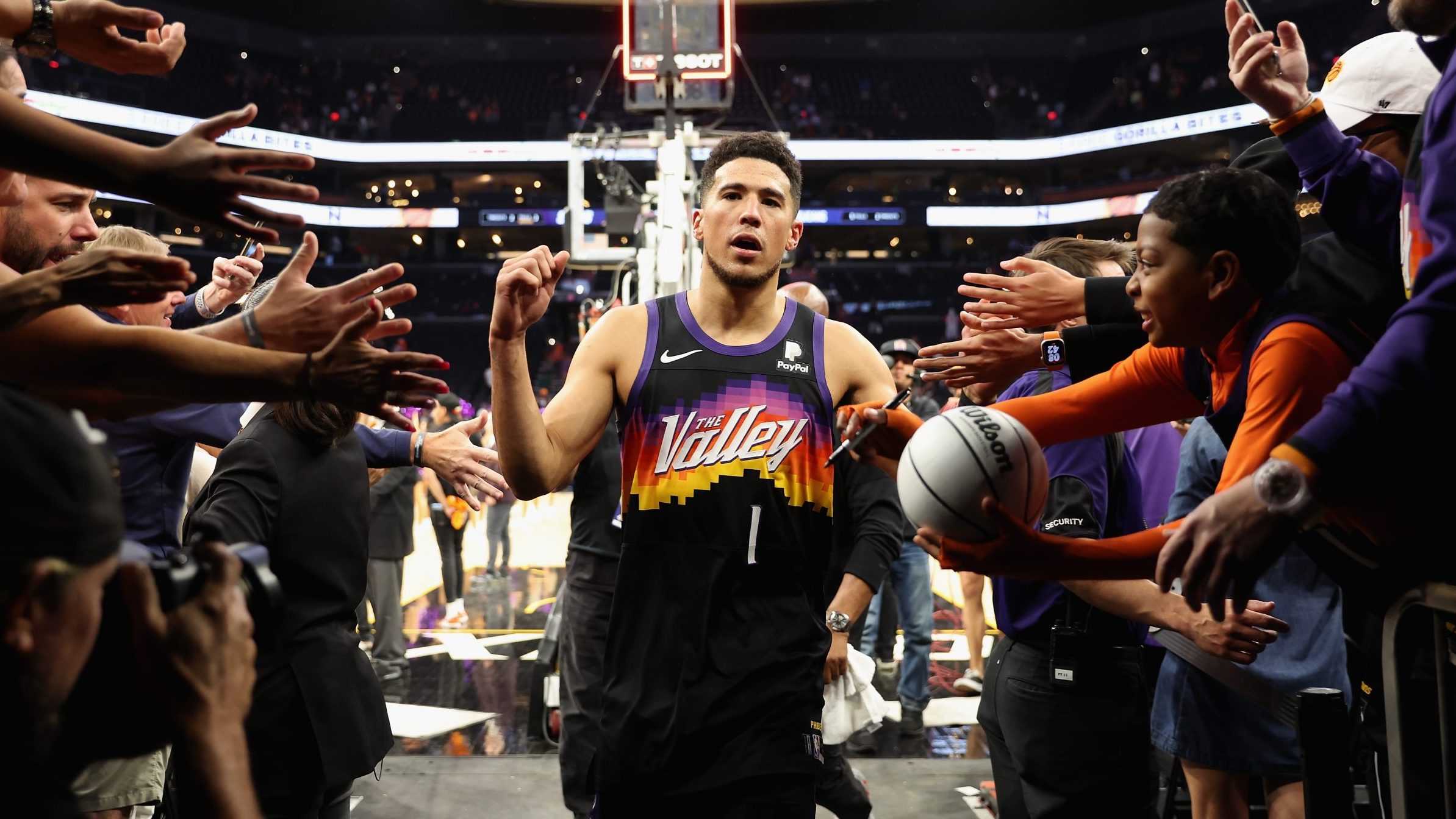 Devin Booker #1 of the Phoenix Suns high fives fans as he walks off the court following game one of...