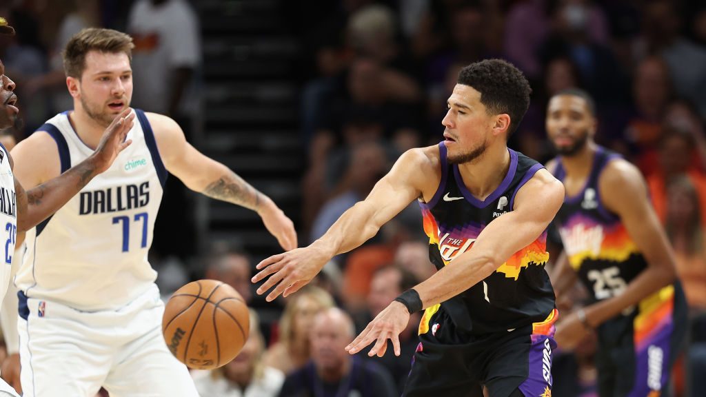 Devin Booker #1 of the Phoenix Suns passes the ball around Luka Doncic #77 of the Dallas Mavericks ...