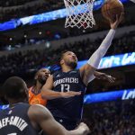 Dallas Mavericks' Dorian Finney-Smith looks on as Jalen Brunson leaps to the basket for a shot after getting past Phoenix Suns forward Jae Crowder, rear, in the second half of Game 4 of an NBA basketball second-round playoff series, Sunday, May 8, 2022, in Dallas. (AP Photo/Tony Gutierrez)