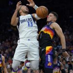 Dallas Mavericks guard Jalen Brunson (13) is blocked by Phoenix Suns guard Devin Booker (1) as he drives to the basket during the first half of Game 2 in the second round of the NBA Western Conference playoff series Wednesday, May 4, 2022, in Phoenix. (AP Photo/Matt York)