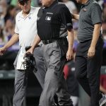 Trainers escort umpire Jerry Layne, center, from his position behind home plate during the sixth inning of a baseball game between the Arizona Diamondbacks and the Colorado Rockies, Saturday, July 2, 2022, in Denver. (AP Photo/David Zalubowski)
