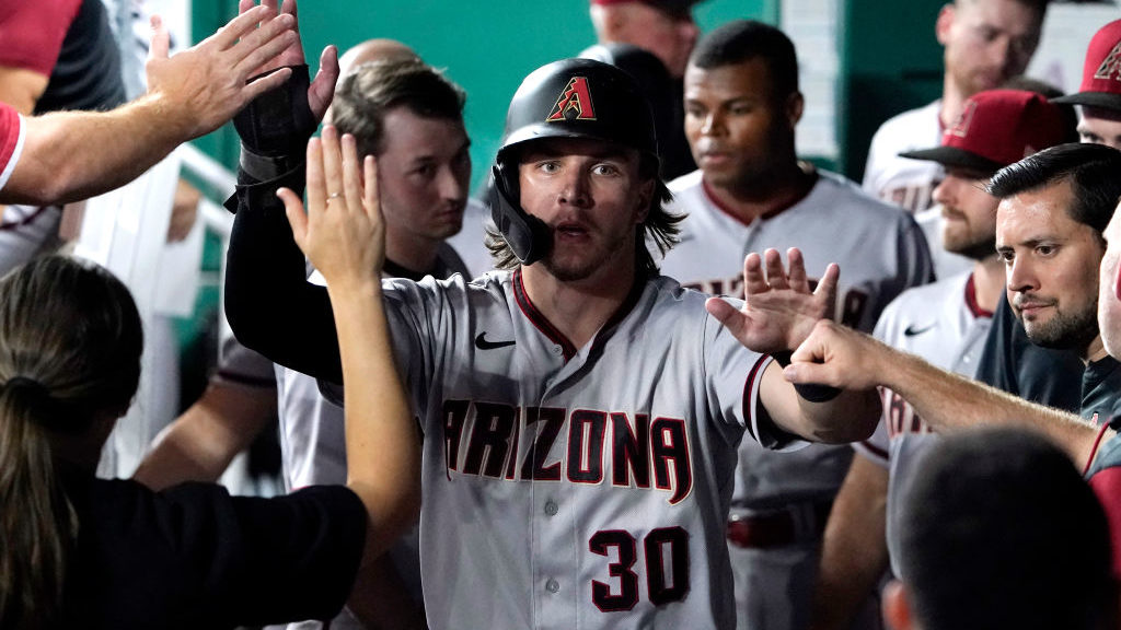 Jake McCarthy #30 of the Arizona Diamondbacks is congratulated in the dugout by teammates after sco...