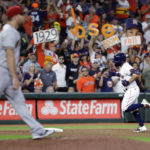 Fans wave signs as Arizona Diamondbacks relief pitcher Ian Kennedy, left, heads to the mound while Houston Astros' Jose Altuve, right, rounds third base on his home run during the sixth inning of a baseball game Tuesday, Sept. 27, 2022, in Houston. (AP Photo/Michael Wyke)