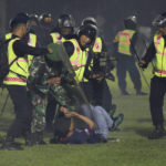 
              Security officers detain a fan during a clash between supporters of two Indonesian soccer teams at Kanjuruhan Stadium in Malang, East Java, Indonesia, Saturday, Oct. 1, 2022. Clashes between supporters of two Indonesian soccer teams in East Java province killed over 100 fans and a number of police officers, mostly trampled to death, police said Sunday. (AP Photo/Yudha Prabowo)
            