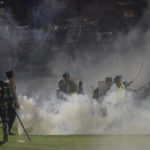 
              Police officers and soldiers stand amid tear gas smoke during a soccer match at Kanjuruhan Stadium in Malang, East Java, Indonesia, Saturday, Oct. 1, 2022. Clashes between supporters of two Indonesian soccer teams in East Java province killed over 100 fans and a number of police officers, mostly trampled to death, police said Sunday. (AP Photo/Yudha Prabowo)
            