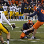 Illinois place kicker Fabrizio Pinton kicks the go ahead field goal off the hold of Hugh Robertson as Iowa defensive back Riley Moss watches during the second half of an NCAA college football game Saturday, Oct. 8, 2022, in Champaign, Ill. Illinois won 9-6. (AP Photo/Charles Rex Arbogast)