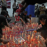 
              Soccer fans light candles and sprinkle flowers during a vigil for the victims of Saturday's stampede, in Tangerang, Indonesia, Tuesday, Oct. 4, 2022. Police firing tear gas inside a stadium in East Java on Saturday in an attempt to stop violence after an Indonesian soccer match triggered a disastrous crush of fans making a panicked, chaotic run for the exits, leaving at a number of people dead, most of them trampled upon or suffocated. (AP Photo/Dita Alangkara)
            