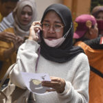 
              A women makes a phone call as she holds a picture of a victim of a soccer riots provided by volunteers for identification purpose, at a hospital in Malang, East Java, Indonesia, Sunday, Oct. 2, 2022. Panic at an Indonesian soccer match Saturday left a number of people dead, most of whom were trampled to death after police fired tear gas to dispel the riots. (AP Photo/Dicky Bisinglasi)
            