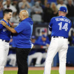 Toronto Blue Jays' Whit Merrifield, left, is checked on by medical staff after being hit by a pitch by Seattle Mariners relief pitcher Diego Castillo during the fifth inning of Game 2 of a baseball AL wild-card playoff series Saturday, Oct. 8, 2022, in Toronto. (Frank Gunn/The Canadian Press via AP)