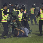 
              Security officers detain a fan during a clash between supporters of two Indonesian soccer teams at Kanjuruhan Stadium in Malang, East Java, Indonesia, Saturday, Oct. 1, 2022. Panic following police actions left over 100 dead, mostly trampled to death, police said Sunday. (AP Photo/Yudha Prabowo)
            