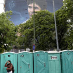 A woman waits her turn to use a toilet in front of a mural of Diego Maradona by artist Martin Ron in Buenos Aires, Argentina, Sunday, Oct. 30, 2022. Sunday marks the birth date of Maradona who died on Nov. 25, 2020 at the age of 60.(AP Photo/Rodrigo Abd)