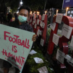 
              A man holds a poster during a candle light vigil for the victims of a deadly crush, outside the Youth and Sports Ministry in Jakarta, Indonesia, Sunday, Oct. 2, 2022. Panic and a chaotic run for exits after police fired tear gas at an Indonesian soccer match in East Java to drive away fans upset with their team's loss left a large number of people dead, most of whom were trampled upon or suffocated. (AP Photo/Dita Alangkara)
            