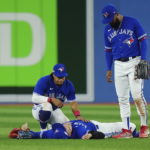 Toronto Blue Jays center fielder George Springer, lays on the field after being injured on a three-RBI double off the bat of Seattle Mariners shortstop J.P. Crawford as Santiago Espinal, left, and Teoscar Hernandez look on during  the eighth inning of Game 2 of a baseball AL wild-card playoff series, Saturday, Oct. 8, 2022, in Toronto. (Nathan Denette/The Canadian Press via AP)