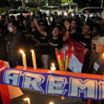 
              Soccer fans chant slogans during a candle light vigil for Arema FC Supporters who became victims of Saturday's soccer riots, outside the Youth and Sports Ministry in Jakarta, Indonesia, Sunday, Oct. 2, 2022. Panic and a chaotic run for exits after police fired tear gas at a soccer match between Arema FC and Persebaya in East Java to drive away fans upset with their team's loss left a large number of people dead, most of whom were trampled upon or suffocated. (AP Photo/Dita Alangkara)
            