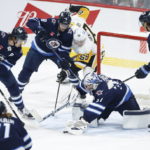 
              Winnipeg Jets goaltender Connor Hellebuyck (37) jumps on the puck as Pittsburgh Penguins' Jake Guentzel (59) attempts to get his stick on the rebound during first-period NHL hockey game action in Winnipeg, Manitoba, Saturday, Nov. 19, 2022. (John Woods/The Canadian Press via AP)
            