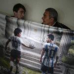 
              Osvaldo Santander and his son Julian pose with a banner illustrated with images of the late soccer legend Diego Maradona and soccer star Lionel Messi, during an interview with The Associated Press in Buenos Aires, Argentina, Thursday, Aug. 18, 2022. Santander and his son Julian will travel to Qatar for the World Cup, their third World Cup as fans. (AP Photo/Natacha Pisarenko)
            