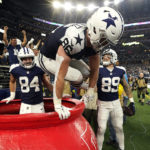 Dallas Cowboys' Dalton Schultz (86) jumps out of a Salvation Army kettle while celebrating Peyton Hendershot's (89) touchdown along with Sean McKeon (84) during the second half of an NFL football game against the New York Giants Thursday, Nov. 24, 2022, in Arlington, Texas. (AP Photo/Tony Gutierrez)