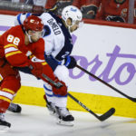 
              Winnipeg Jets defenseman Dylan DeMelo, right, and Calgary Flames forward Andrew Mangiapane chase the puck during the second period of an NHL hockey game Saturday, Nov. 12, 2022, in Calgary, Alberta. (Jeff McIntosh/The Canadian Press via AP)
            