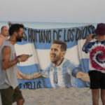 Argentina soccer fans takes a photo with a banner showing the image of Argentina's Lionel Messi at a beach in Al Wakrah, Qatar, Sunday, Nov. 27, 2022. The World Cup soccer tournament is being held from Nov. 20 to Dec. 18 in Qatar. (AP Photo/Lee Jin-man)