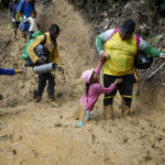 
              A woman lifts a child from a muddied path as Ecuadorian migrants walk across the Darien Gap from Colombia into Panama hoping to reach the U.S., on Oct. 15, 2022. (AP Photo/Fernando Vergara)
            