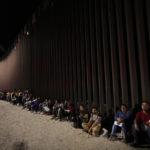 
              Migrants wait along a border wall after crossing from Mexico, near Yuma, Ariz., on Aug. 23, 2022. (AP Photo/Gregory Bull)
            