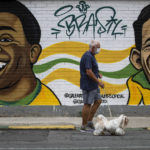 
              A man walks his dog past a mural of Brazilian soccer stars Pele, left, and Garrincha in Rio de Janerio, Brazil, Friday, Dec. 30, 2022. Edson Arantes do Nascimento, known to the world as Pele, died in Sao Paulo Thursday at the age of 82. (AP Photo/Bruna Prado)
            