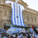 A giant jersey of the Argentine national soccer team hangs on the front of the Colon Theater as fans celebrate their team's World Cup victory over France in Buenos Aires, Argentina, Sunday, Dec. 18, 2022. (AP Photo/Gustavo Garello)