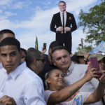 
              Brazil's President Jair Bolsonaro, center, poses for a selfie with a supporter as he campaigns for reelection at the rural workers' settlement New Jerusalem, in Brasilia, Brazil, on Oct. 24, 2022. (AP Photo/Eraldo Peres)
            